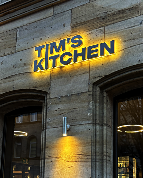TIM'S KITCHEN Logo beleuchtet an einer Fassade