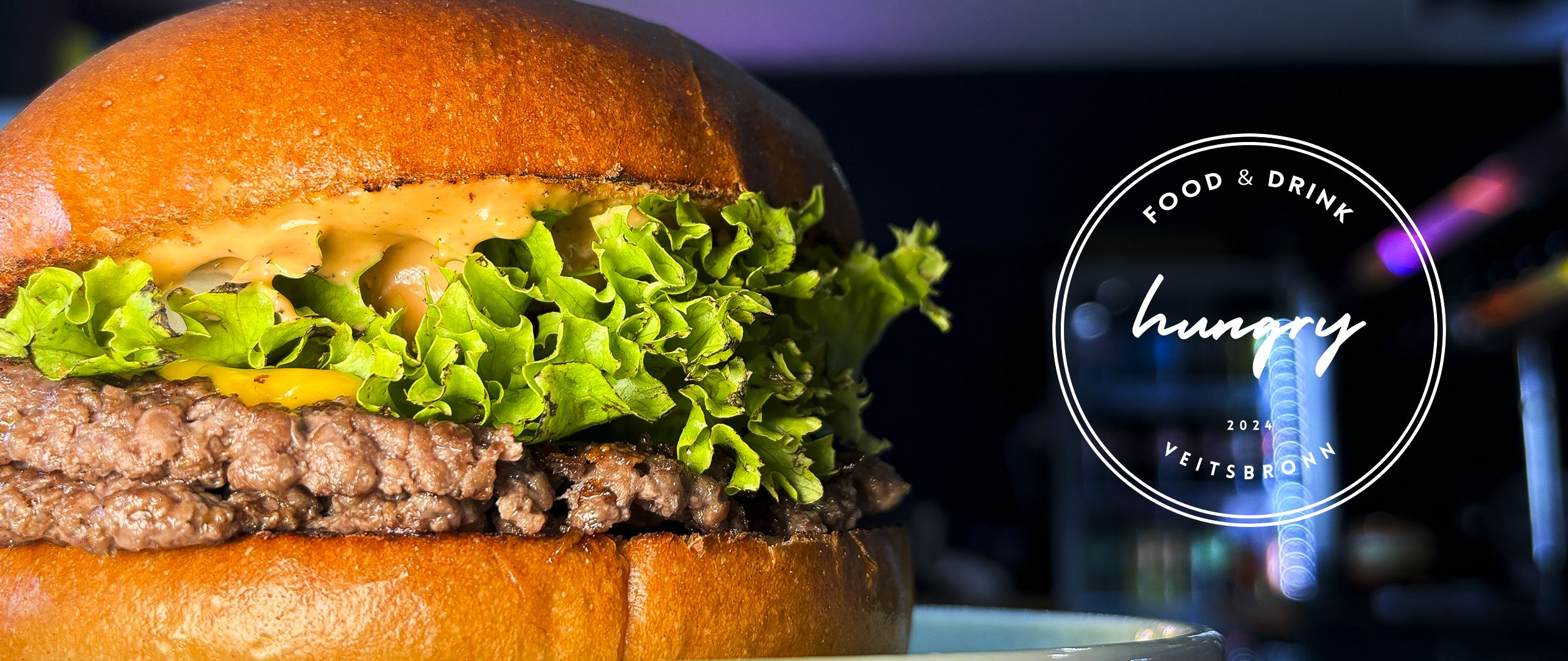 Close-up Bild von einem Burger und daneben das hungre Veitsbronn Logo